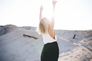 Woman at the beach putting arms in the air as if she is happy about something.